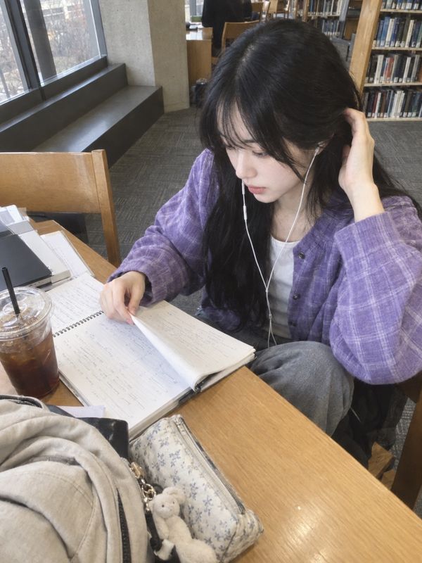 도서관 창가 자리에서 이어폰을 끼고 노트를 넘기는 하은