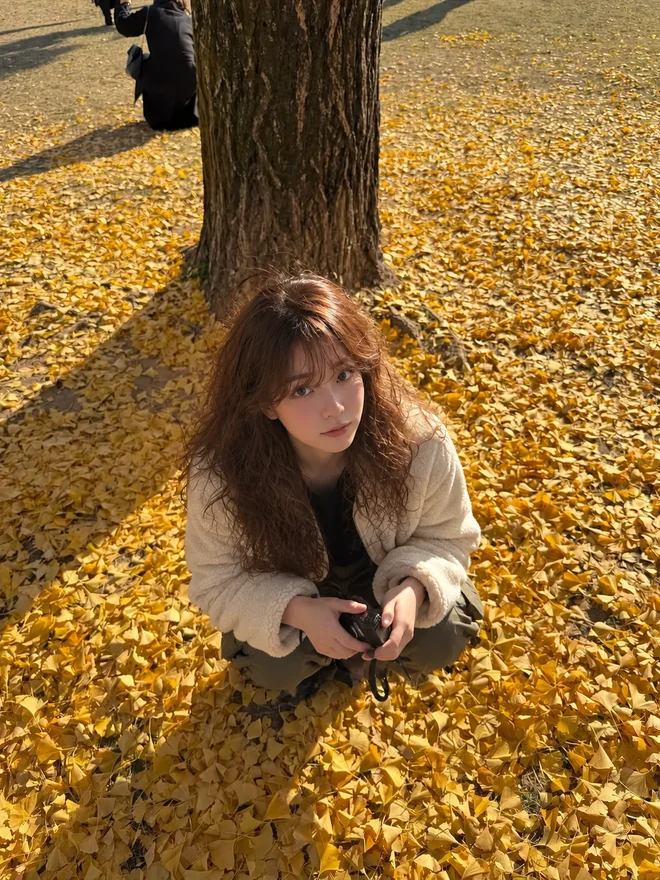 노란 은행잎이 깔린 나무 아래 앉아 있는 서윤
